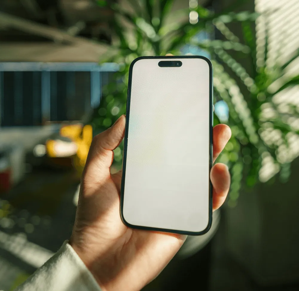 A hand holding up a phone among green leaves