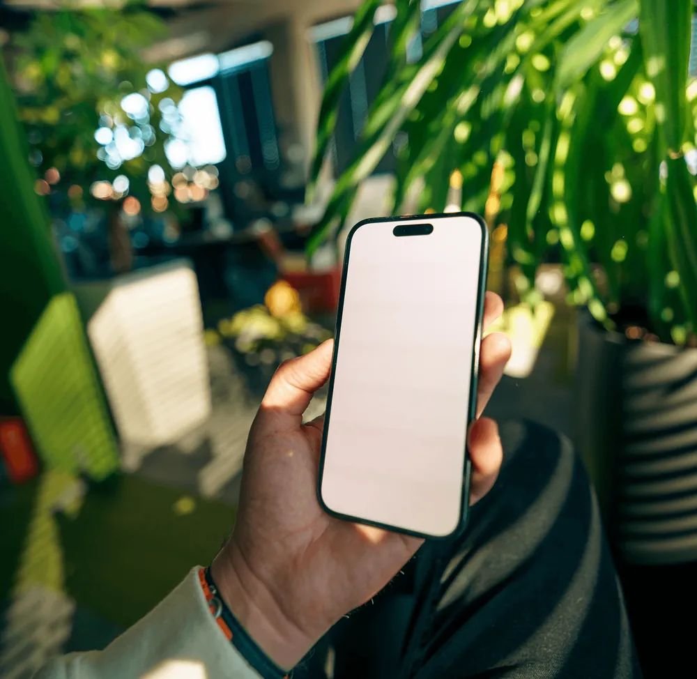 A hand holding a phone with a blank screen in front of leaves