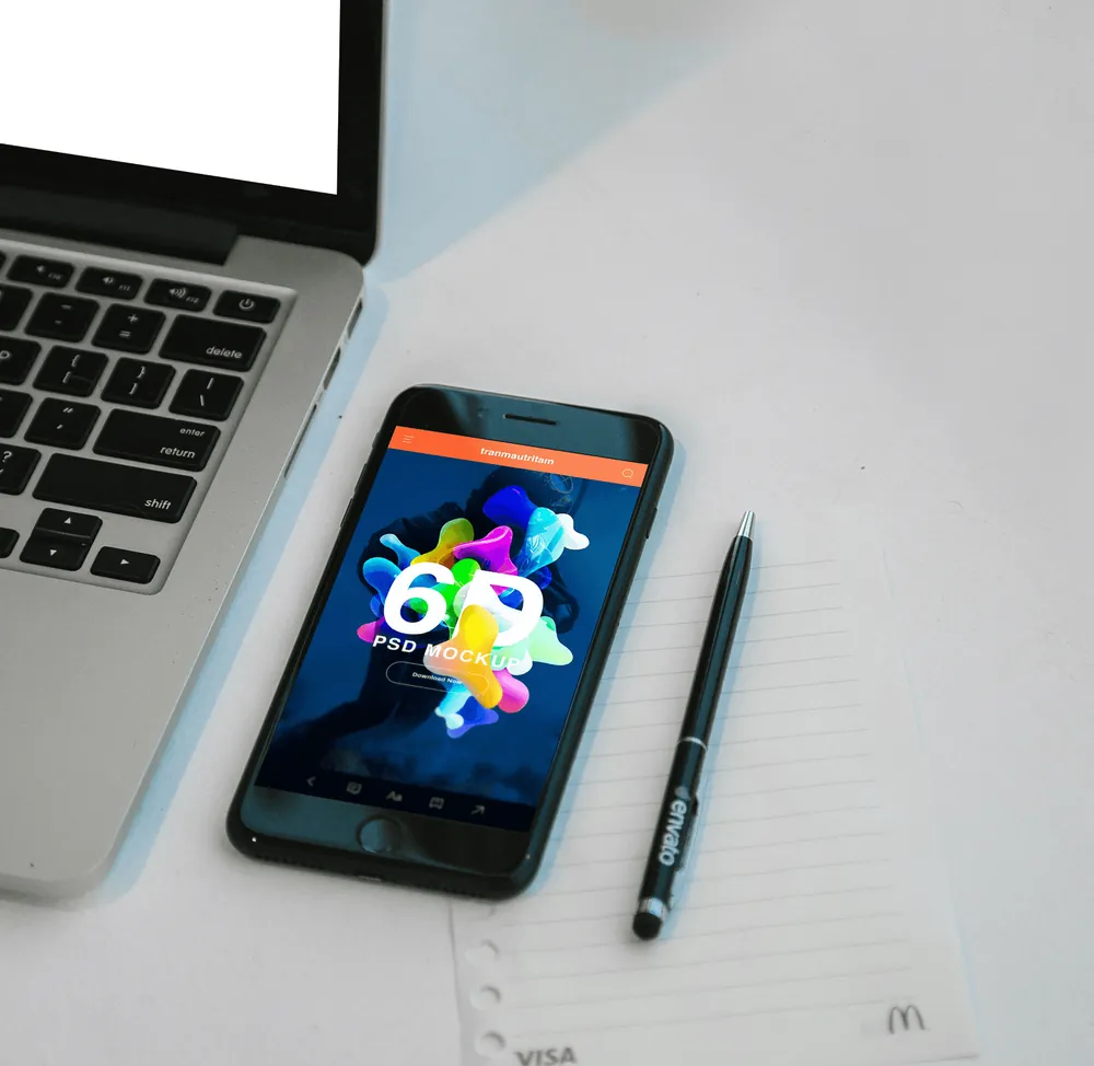 A phone with a colourful app screen beside a laptop and a pen