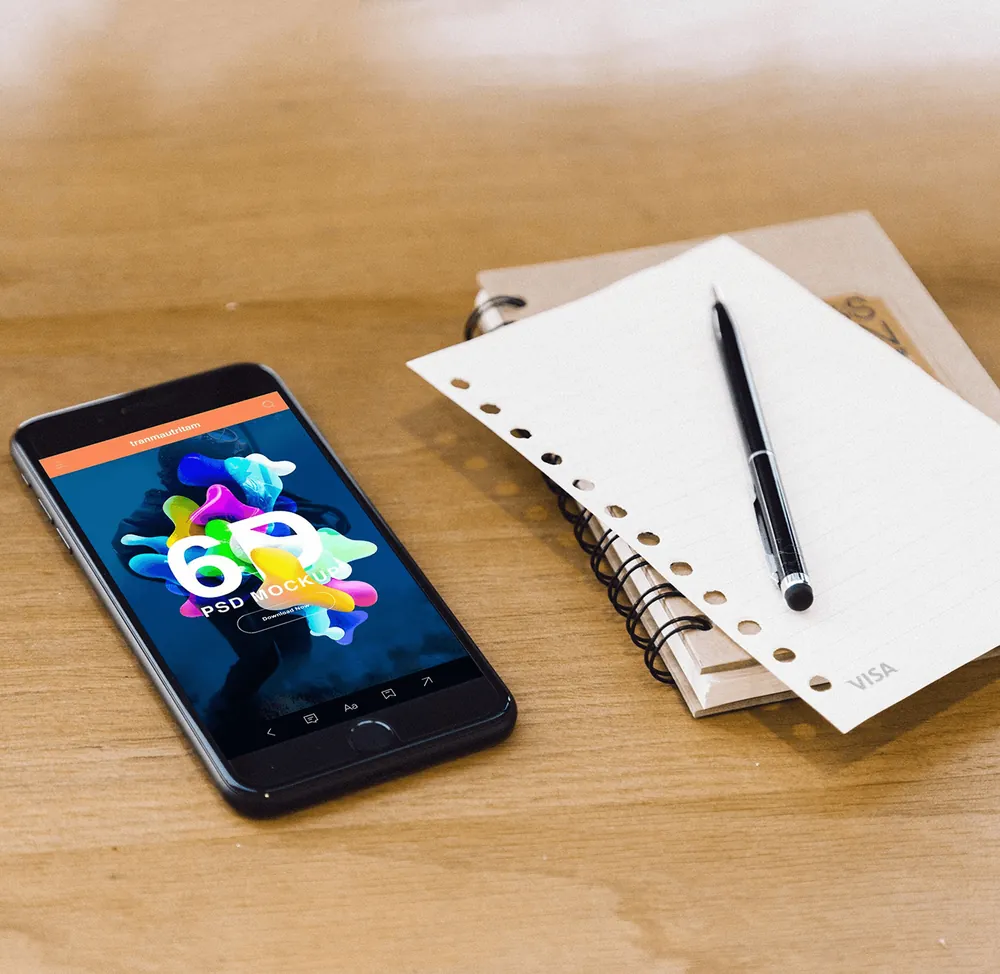 Smartphone with a colourful app screen on a wooden desk beside a spiral notebook and pen