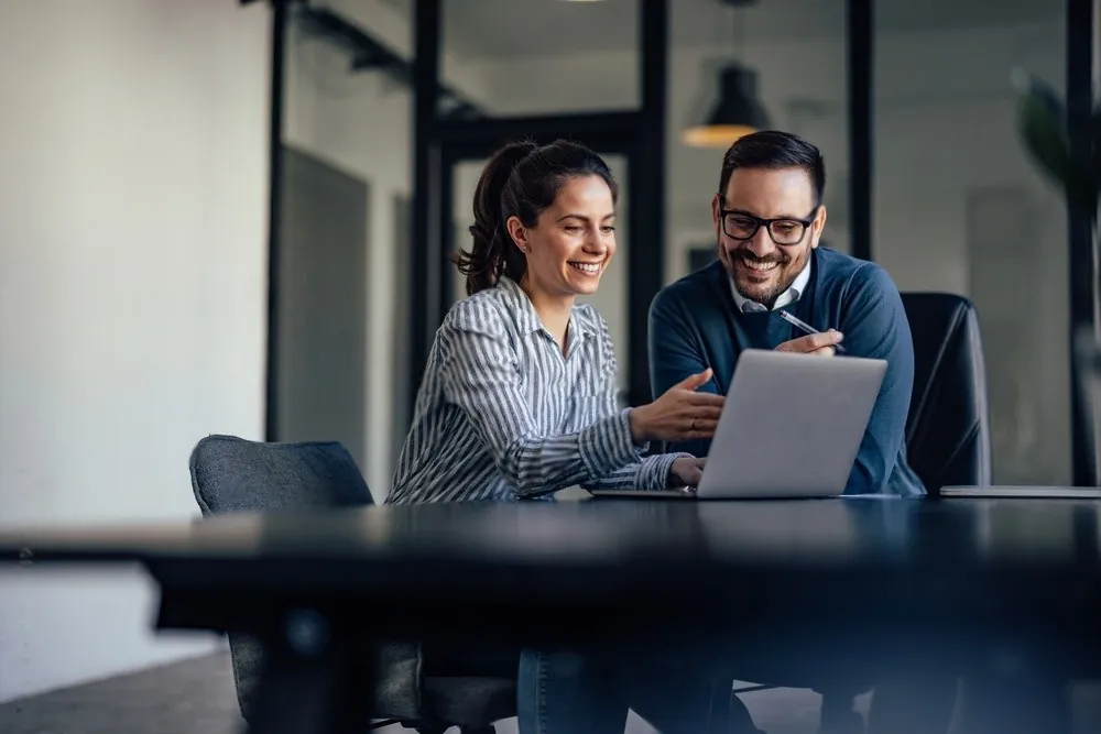 Two colleagues at a laptop in a dark office