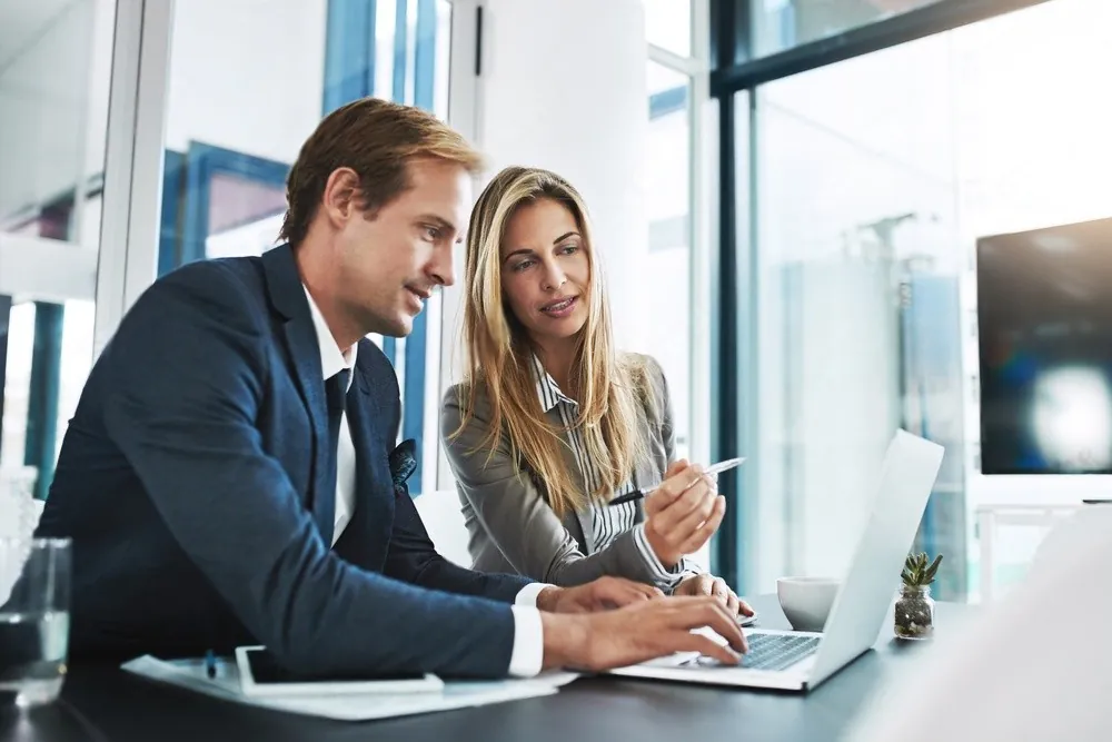 Two colleagues at a laptop by a window