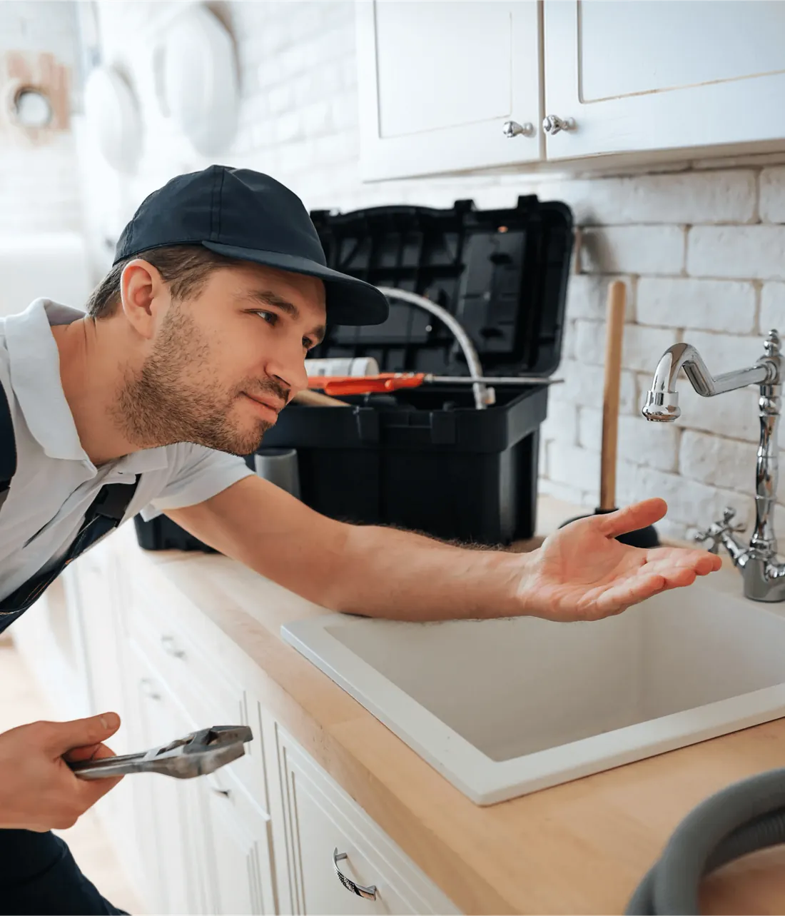 A plumber checking a kitchen tap with a pair of pliers, his toolbox on the counter