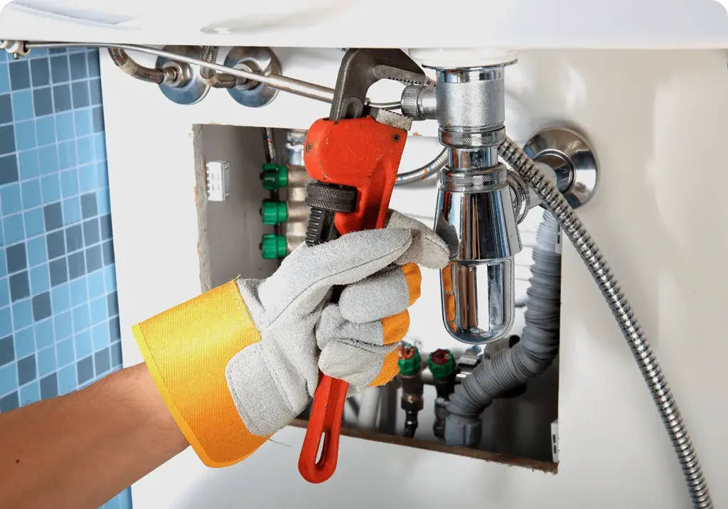 A plumber in yellow gloves loosening pipes under a sink