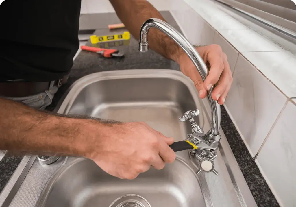 A hand turning a kitchen tap over a steel sink