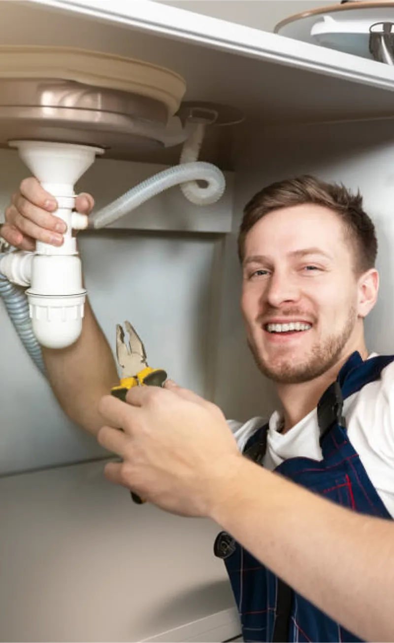A smiling plumber fitting a drain pipe under a bathroom sink