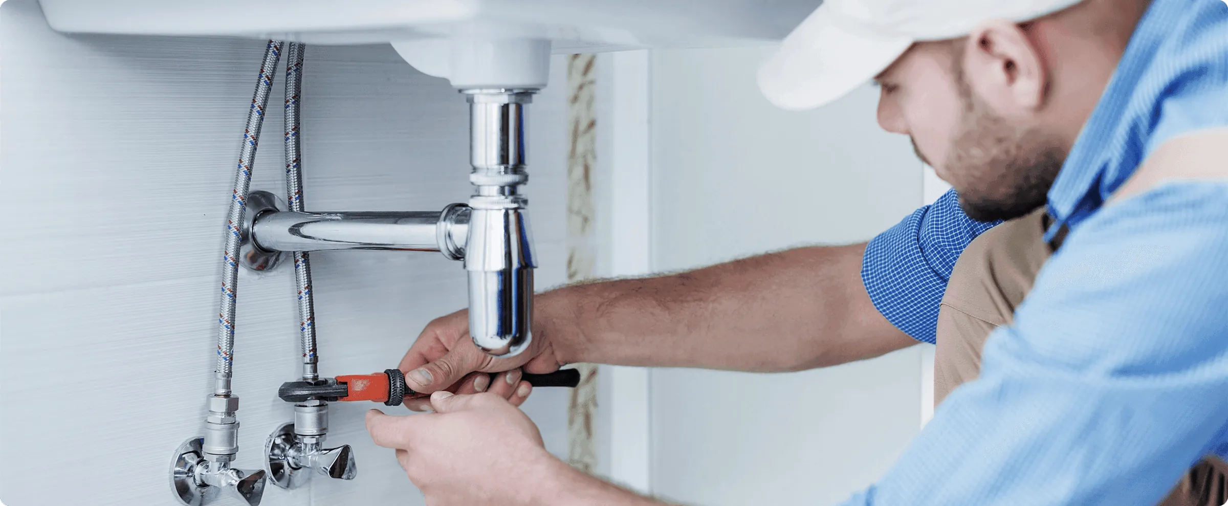 A plumber loosening a sink trap with a red wrench