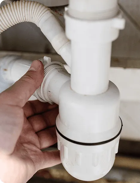 A plumber cleaning a white sink drain trap
