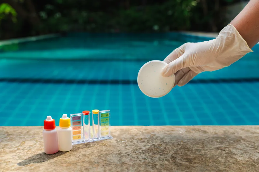 A gloved hand holding a chlorine tablet next to a water test kit