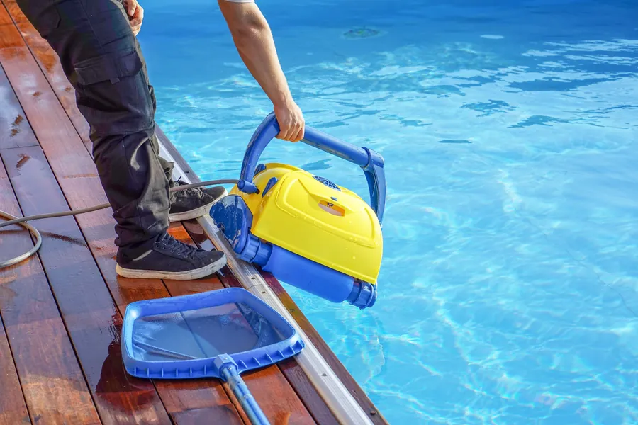A robotic pool cleaner and a skimmer net beside a blue pool