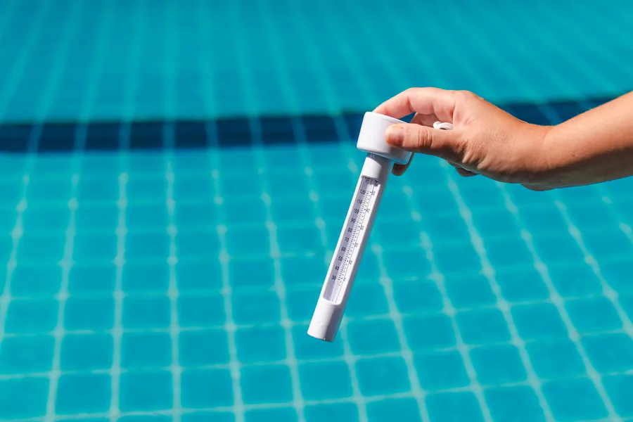 A hand holding a water tester above a tiled pool