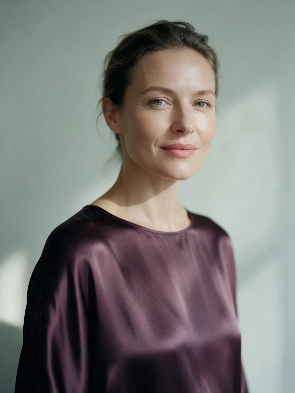 A woman in a plum satin top looking calmly into the camera in soft daylight