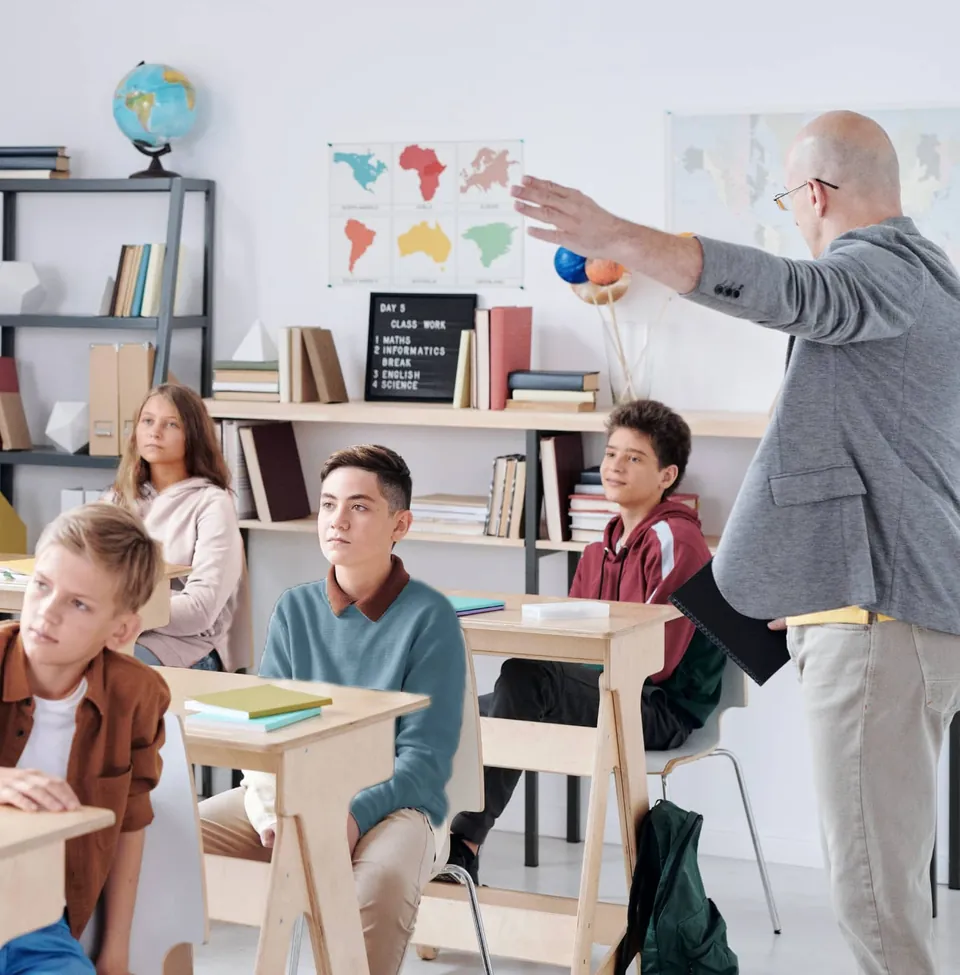 A teacher pointing at a world map in a classroom