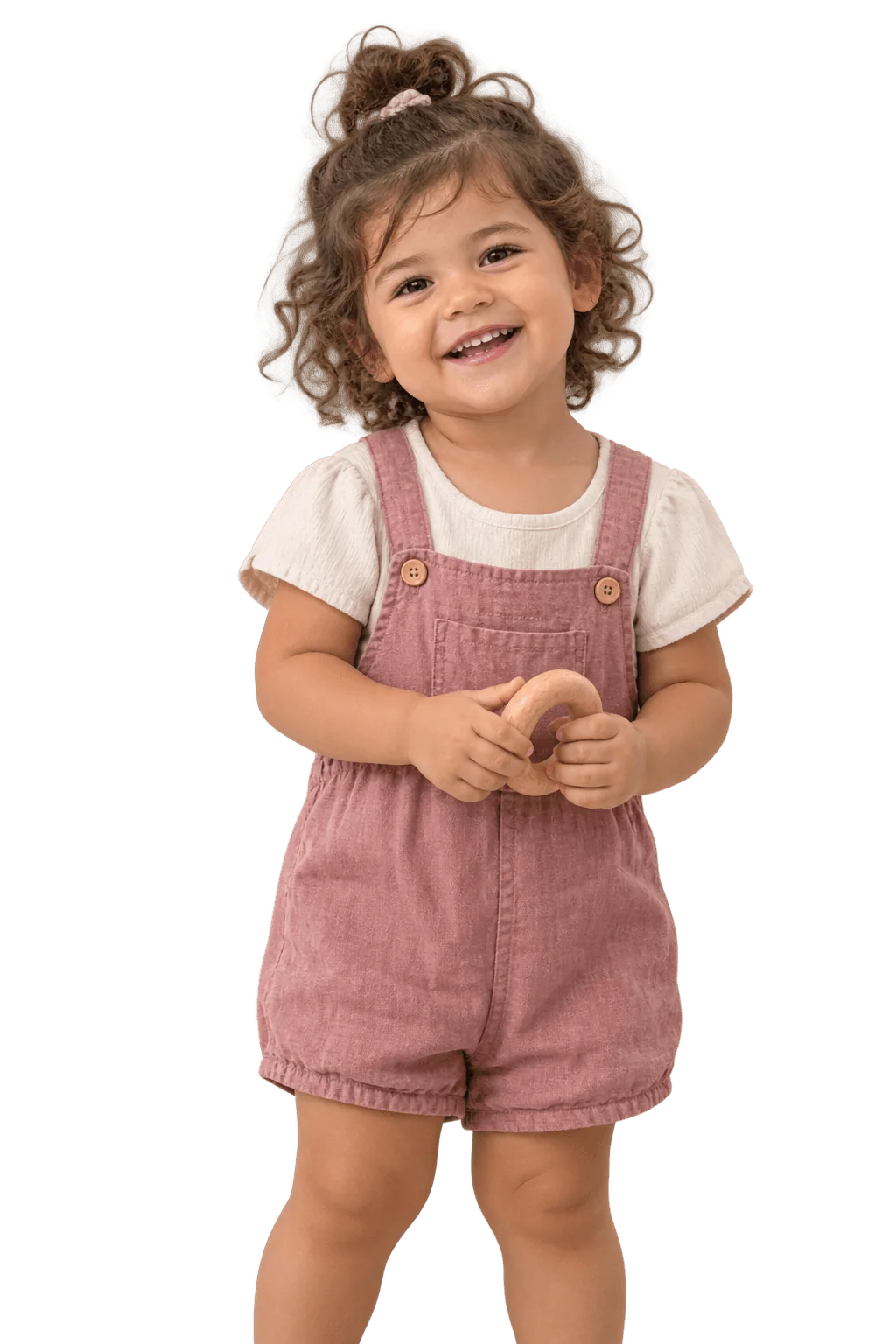 A smiling toddler in pink overalls holding a wooden ring