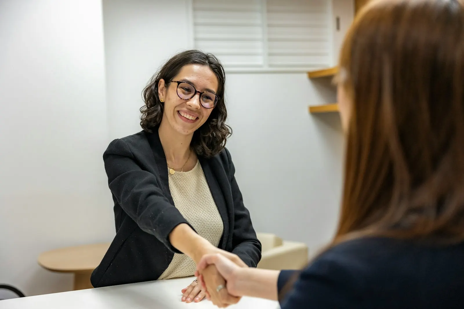 Two women shaking hands across a desk