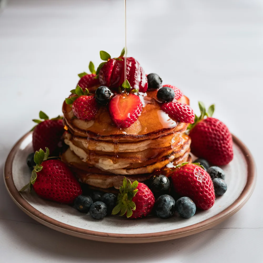 A stack of pancakes topped with strawberries and blueberries