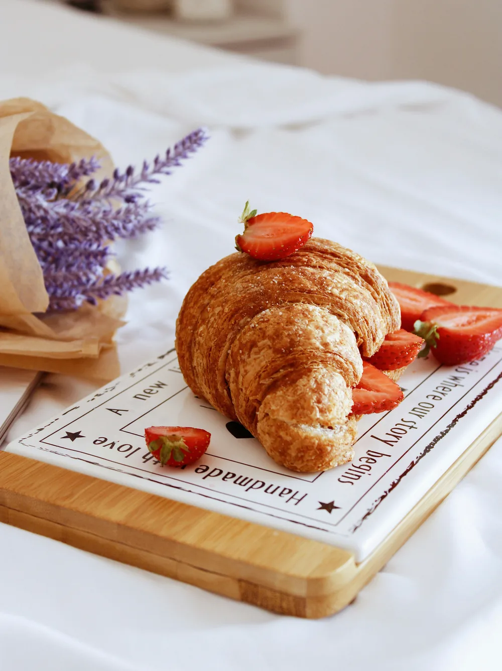 A croissant with fresh strawberries on a wooden board