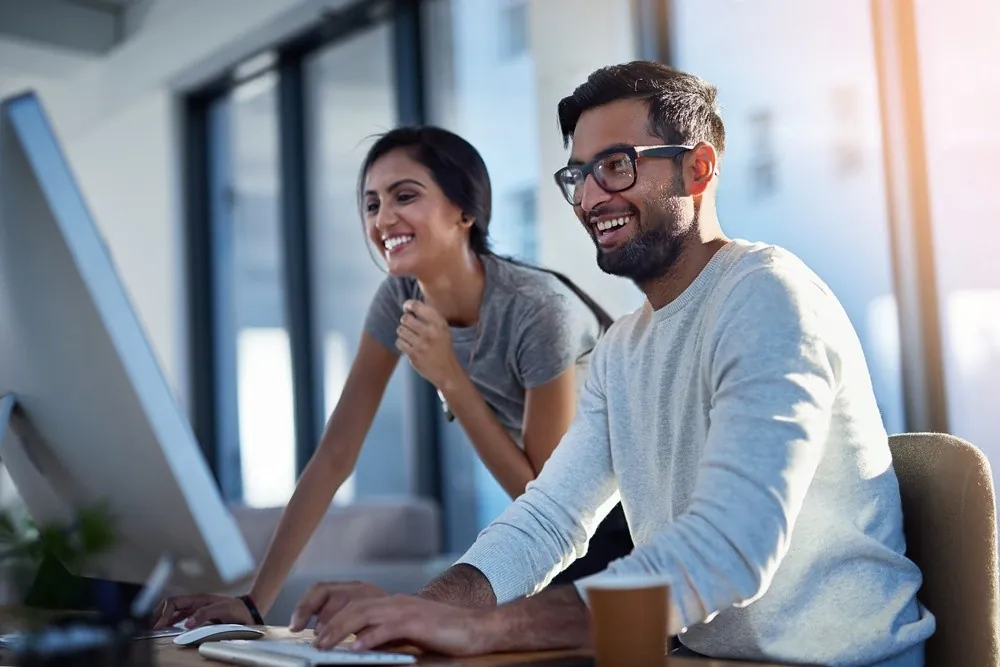 Two colleagues smiling at a laptop