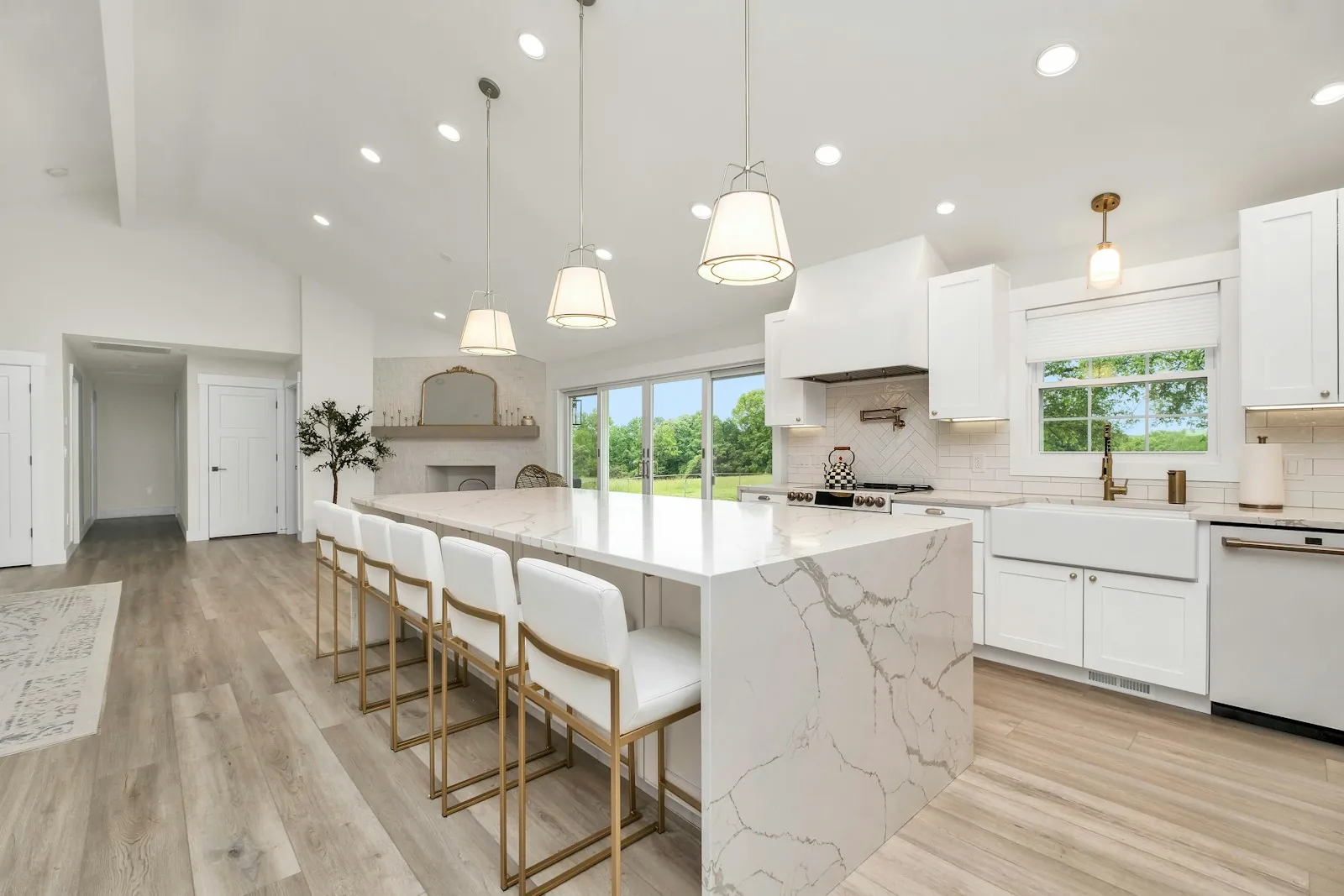 A white kitchen with a marble island and pendant lights