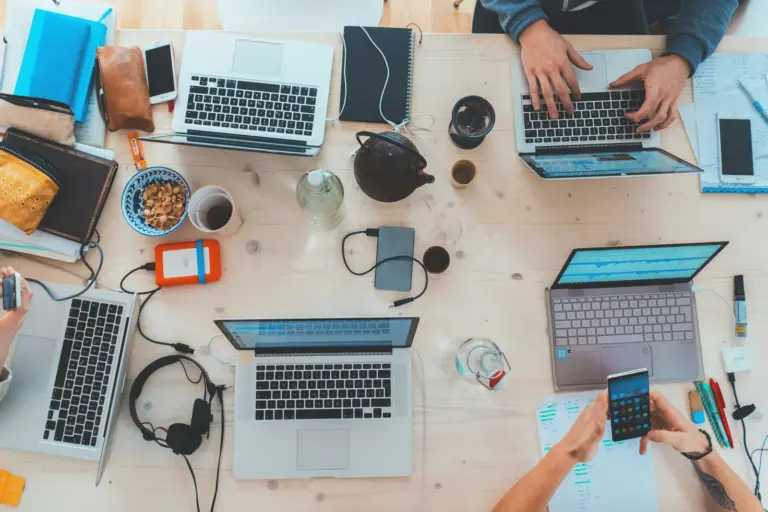 Laptops, phones and coffee on a shared table seen from above