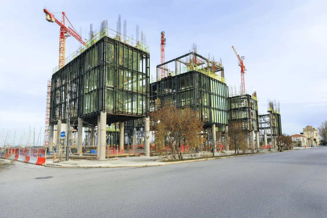 A glass building under construction beside tall cranes