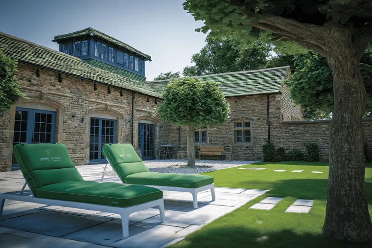 Green lounge chairs on a lawn beside a stone house