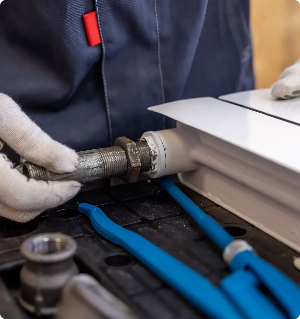 Gloved hands tightening a threaded pipe joint next to blue pipe tools