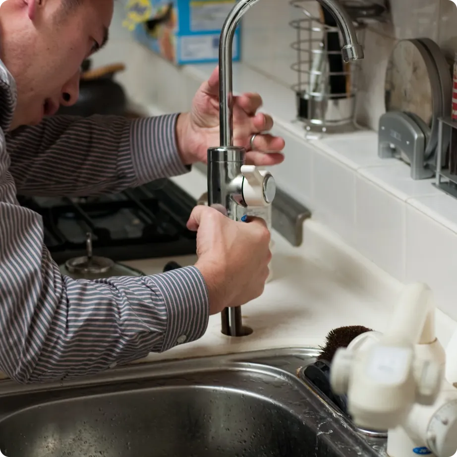 Plumber fitting a kitchen tap in a tidy home kitchen