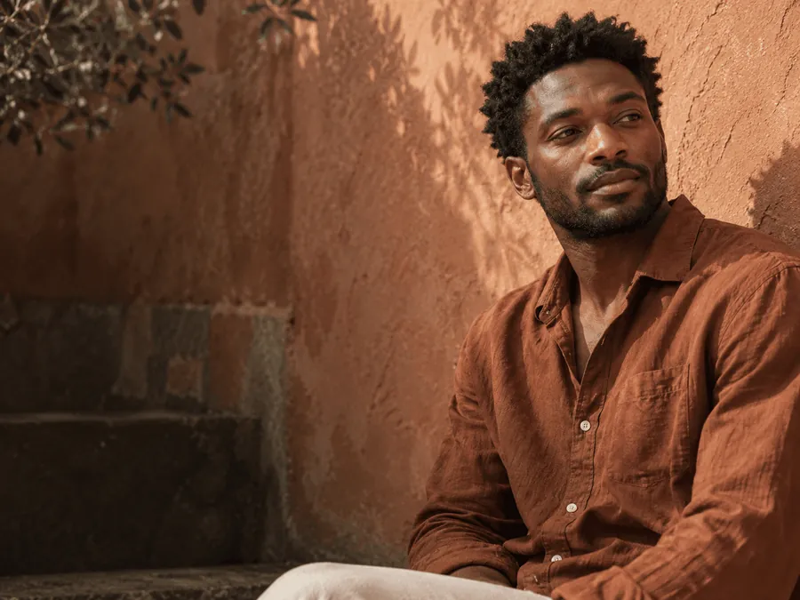 A man in a rust shirt sitting beside a terracotta wall