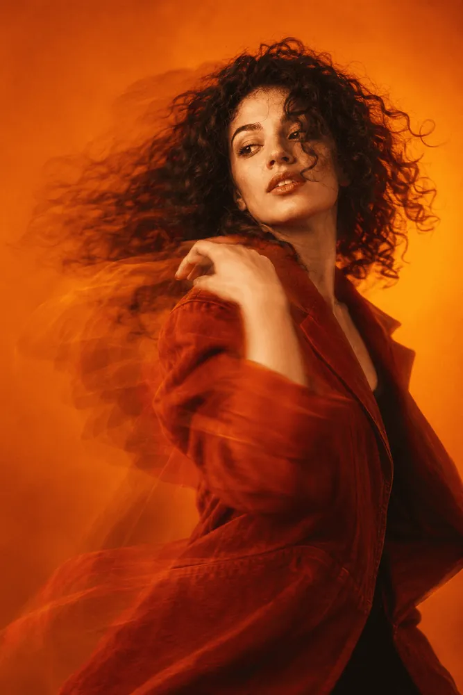 Editorial portrait in an orange jacket, caught mid-movement