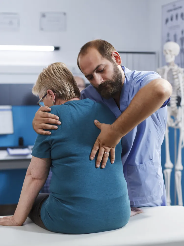 A chiropractor examining the back of an older patient seated on the treatment table