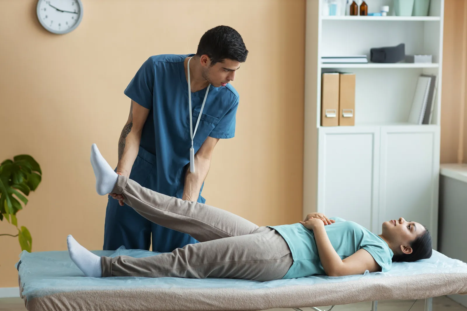 A physiotherapist stretching the leg of a patient lying on a treatment table