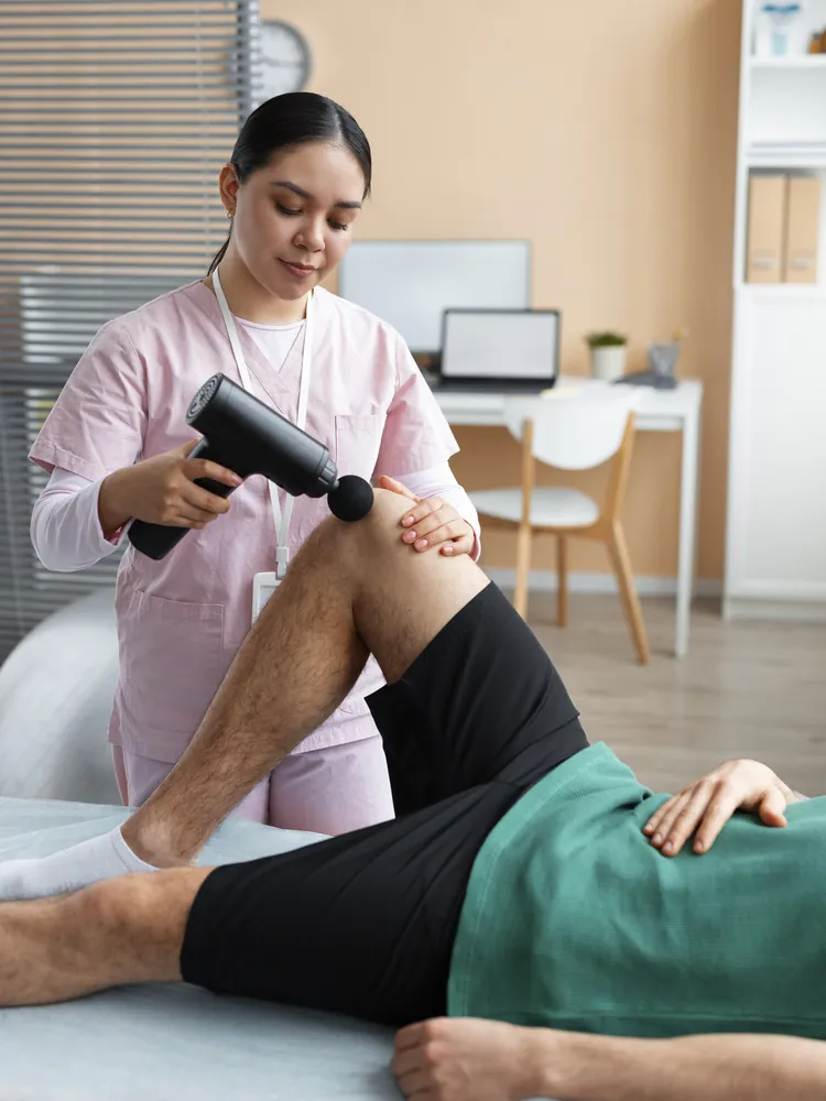 A physiotherapist treating a patient’s leg with a massage gun