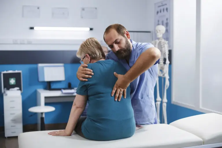 A chiropractor checking the posture of an older patient seated in the clinic