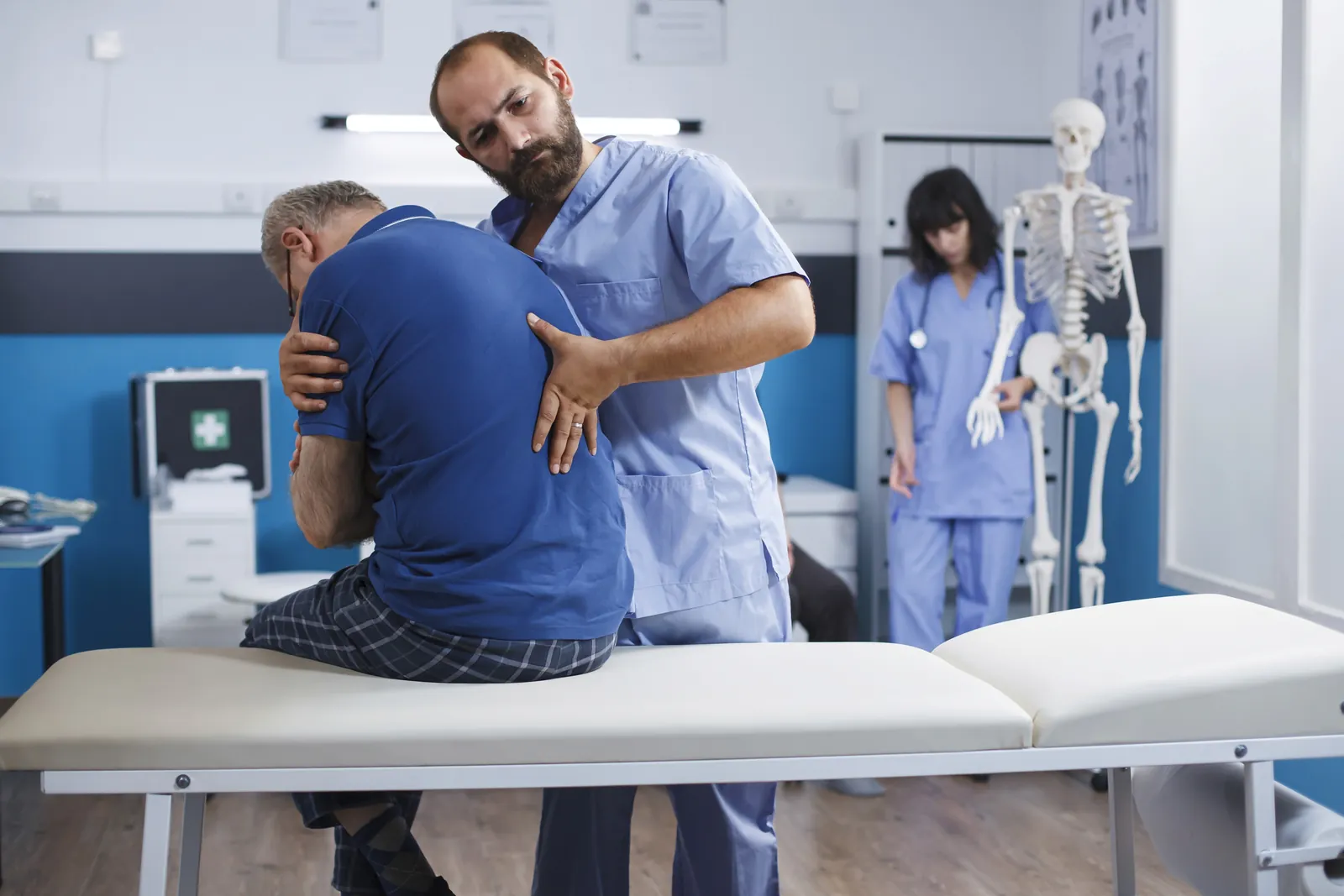 Two clinicians helping a patient sit up on a treatment table during a rehabilitation session