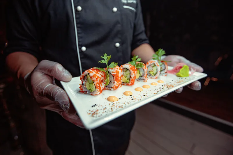 A chef in black gloves holding a plate of rolls