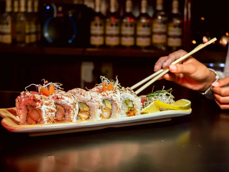 Chopsticks lifting a roll from a long plate of sushi