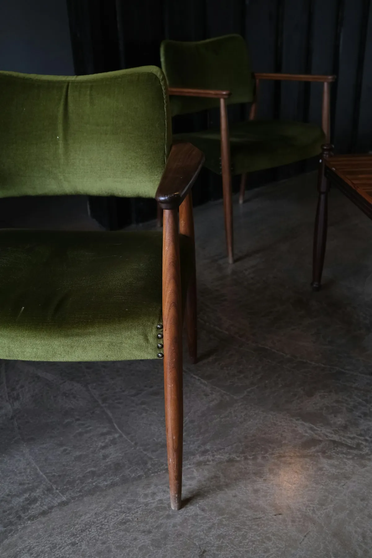 Two green velvet dining chairs on a dark stone floor
