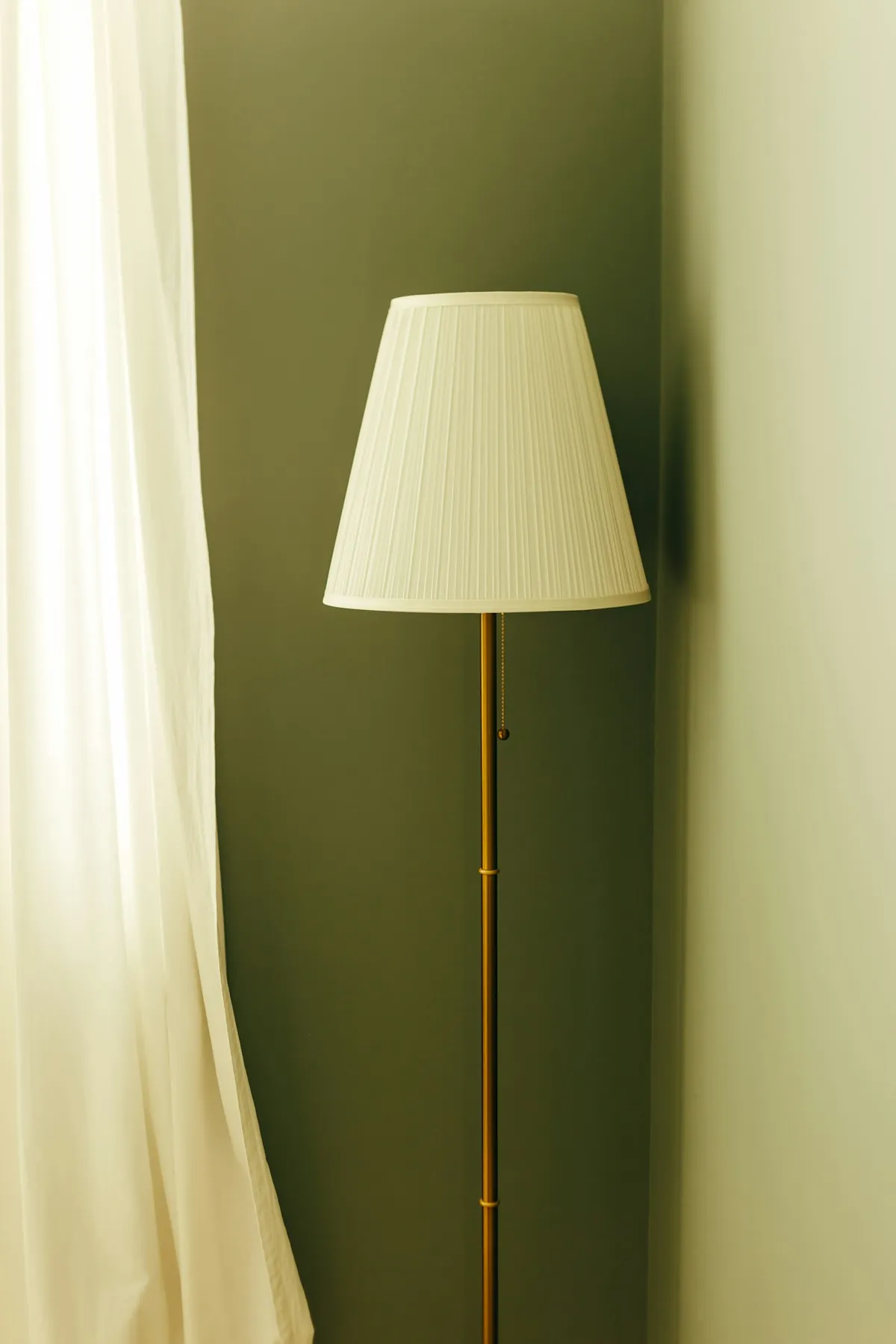 A tall brass floor lamp against an olive green wall