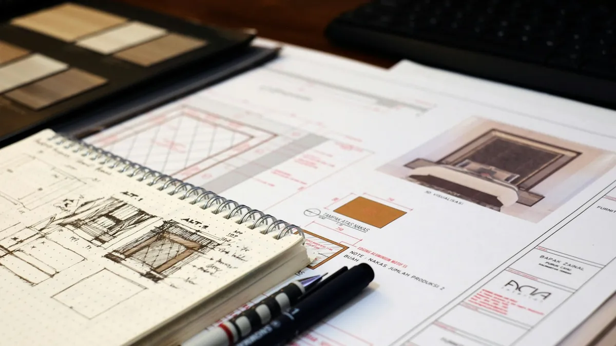 A sketchbook with an interior drawing on a desk, next to fabric and tile samples and a printed design board