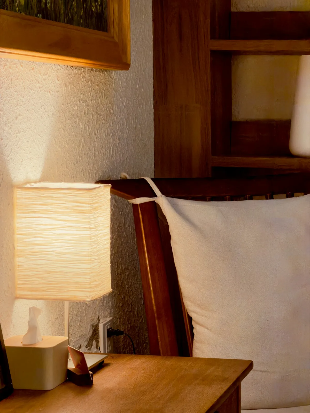 A bedside lamp with a paper shade glowing on a wooden table