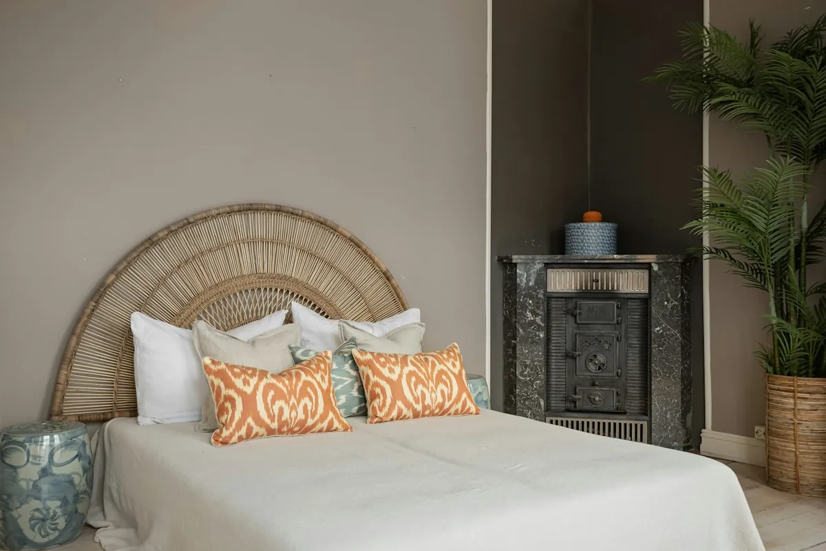 A bed with a round rattan headboard and orange patterned cushions