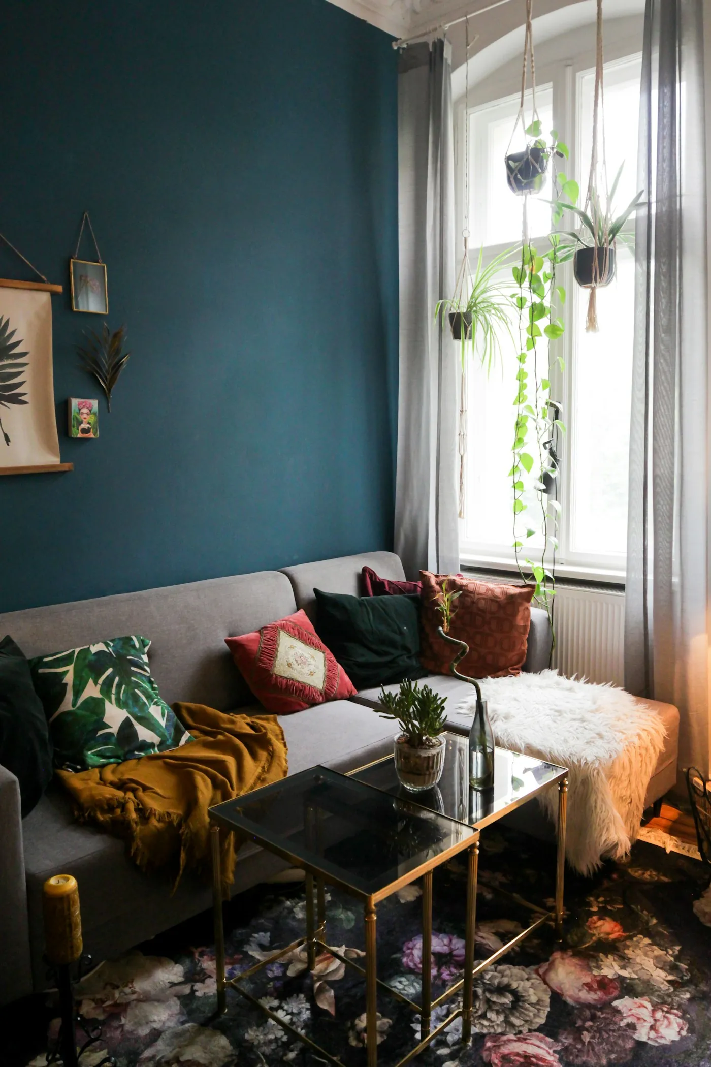 A living room with deep teal walls, a cream sofa with mustard and green cushions, and plants on the window sill