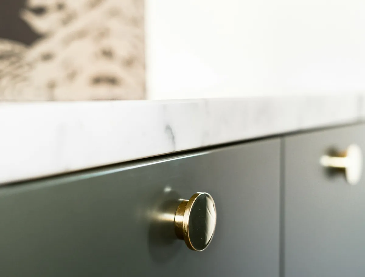 A close-up of a round brass knob on a green cupboard door