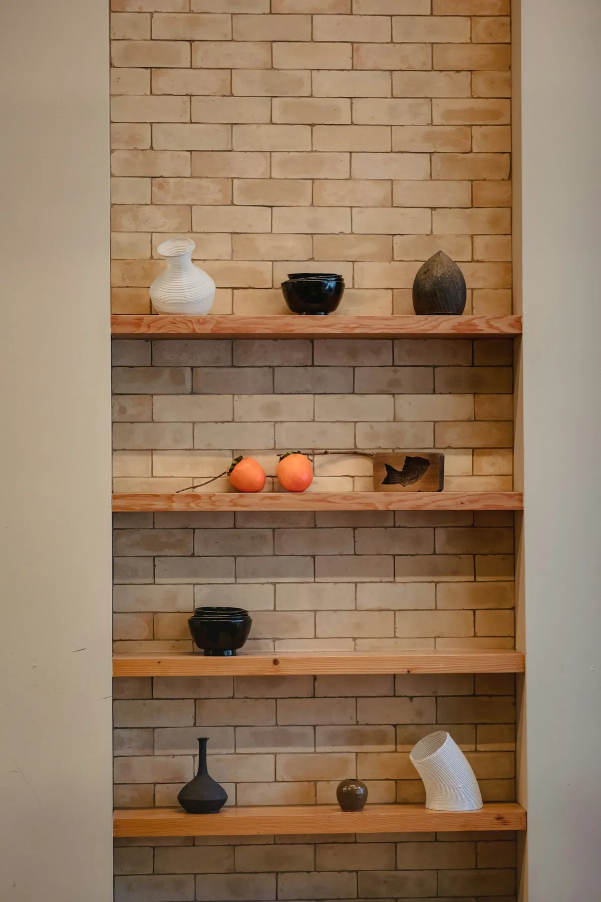 Ceramic vases on wooden shelves built into a brick alcove