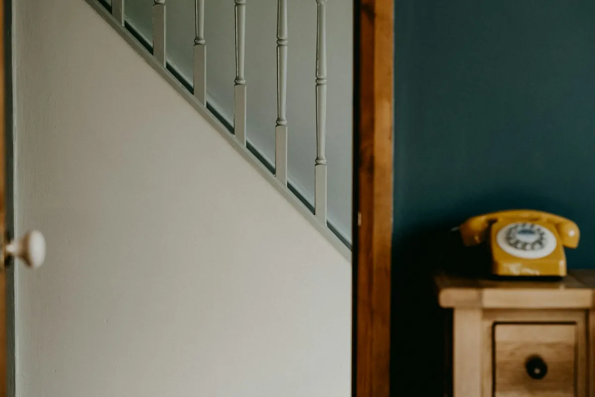 A teal wall beside a staircase, with a yellow telephone on a wooden table