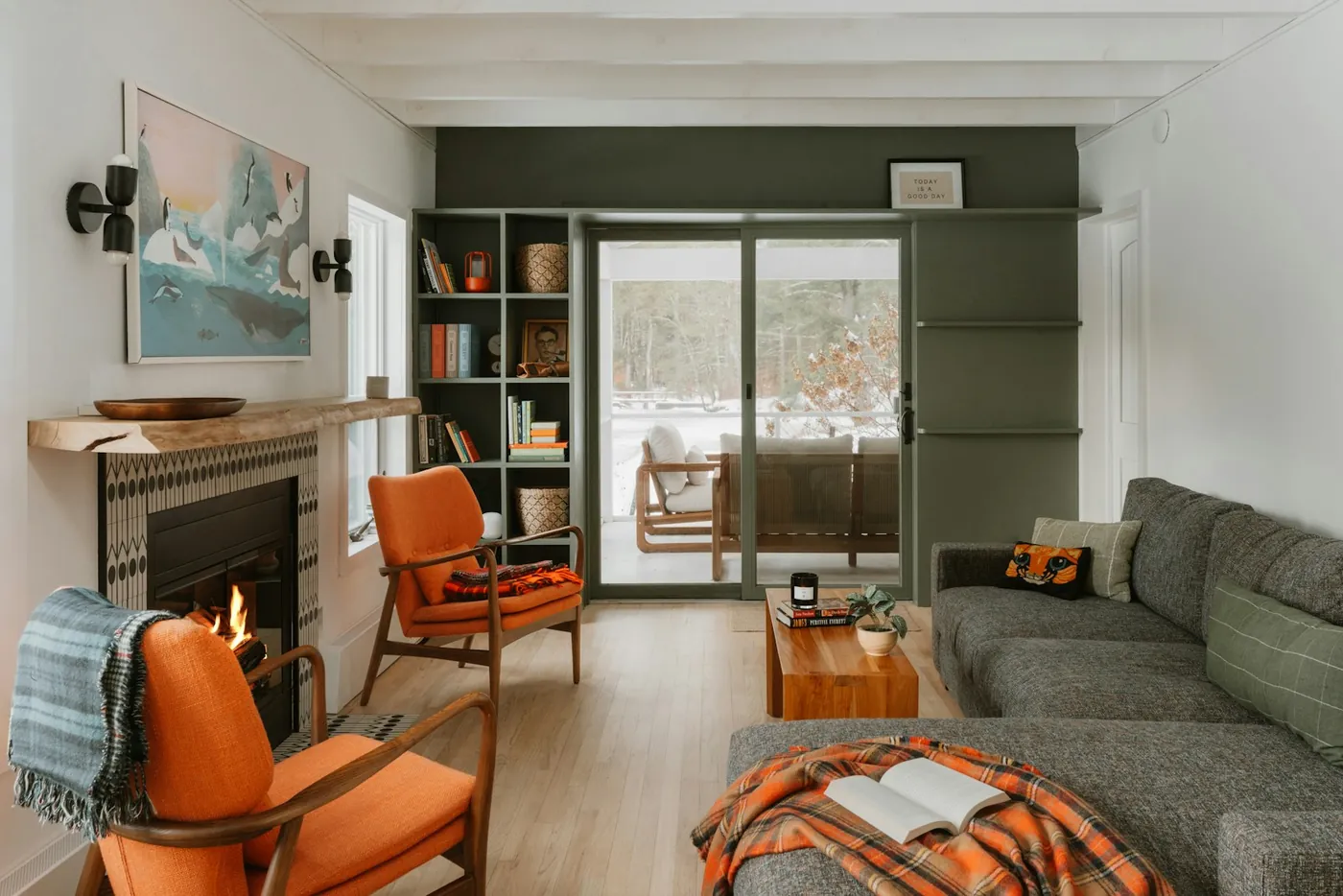 A living room with two orange armchairs, a fireplace, an olive green wall and full bookshelves