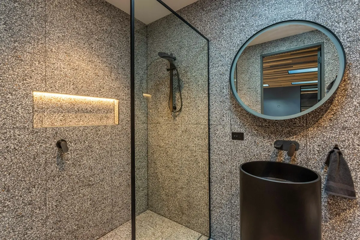 A walk-in shower with a lit niche and terrazzo walls