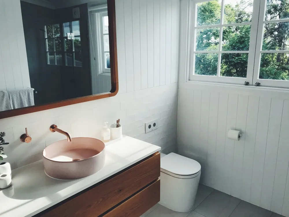 A pink basin on a wooden vanity in a bathroom with white panelled walls