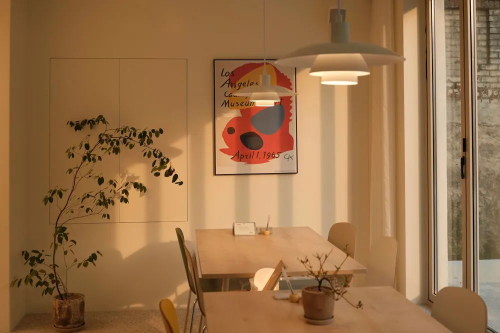 A warm dining room with a pale wooden table, a red print on the wall and a pendant light